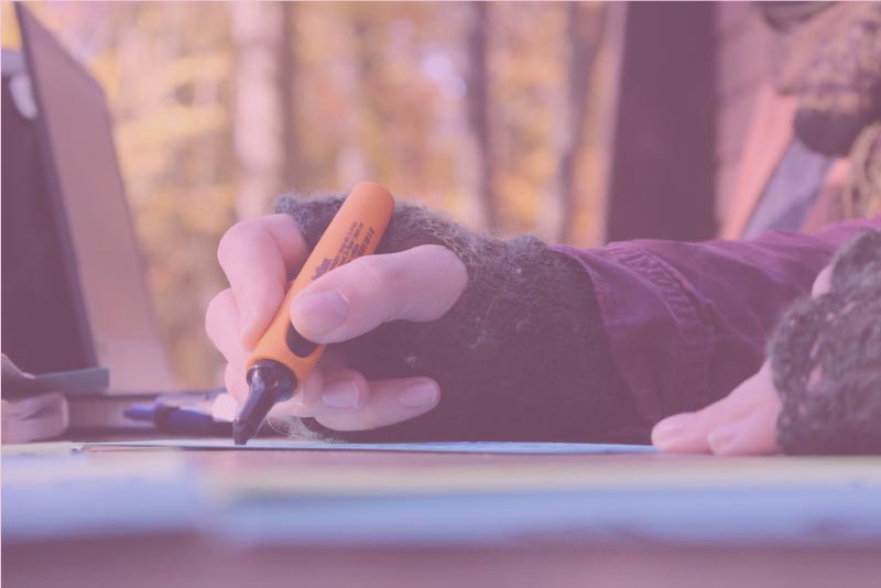 schreibt-uns-wenn-ihr-Fragen-zu-unserer-Klima-Bildungsarbeit-habt Eine Hand schreibt mit einem Stift auf ein Blatt Papier.